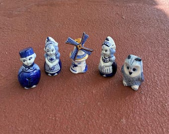May include: A collection of blue and white ceramic figurines. The set includes a Dutch boy, two Dutch girls, a windmill, and an owl. The figurines are detailed with traditional Dutch clothing and windmill design.