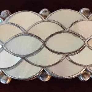 May include: A silver-toned bracelet with a repeating pattern of iridescent, shell-like segments. The segments are cream-colored with a pearlescent sheen, and are outlined with silver metal. The bracelet has a curved shape and is designed to fit the wrist.