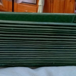 May include: A dark green rectangular planter with horizontal striped detailing. The planter has a slightly flared shape and a solid base. The interior is a solid dark green. Suitable for indoor or outdoor use.