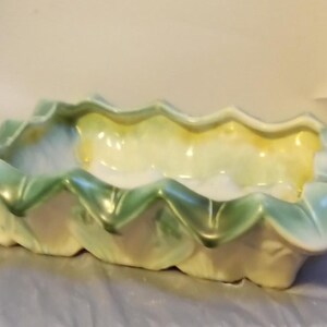 May include: A rectangular ceramic planter with a scalloped edge. The planter is painted in shades of green, yellow, and white. The design resembles a flower or leaf shape. The planter is suitable for indoor or outdoor use.