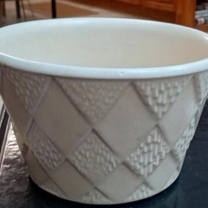 May include: Cream-colored ceramic planter with a textured diamond pattern. The planter has a wide, rounded rim and a slightly tapered shape. The diamond pattern is made up of alternating textured and smooth squares.