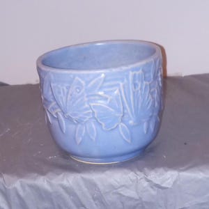 以下が含まれることがあります： 蝶と葉のレリーフ模様が施された薄い青色のセラミック製のプランター