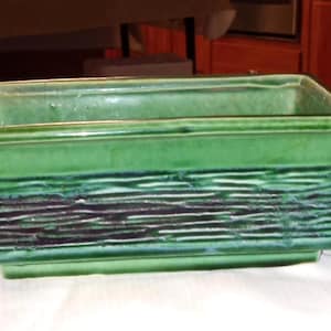 以下が含まれることがあります： テクスチャ加工された水平ストライプのデザインが施された、長方形の緑色のセラミックプランター。 プランターは光沢仕上げで、屋内または屋外での使用に適しています。 プランターの長さは約30cmです。