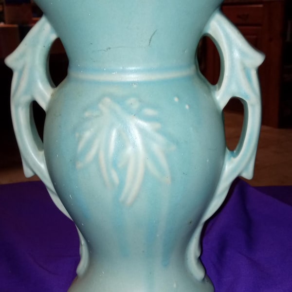 Peut inclure: Un vase en céramique bleu clair avec deux anses et un dessus évasé. Le vase présente un motif de feuilles dans une nuance de bleu plus claire. Le vase mesure environ 25 cm de haut.