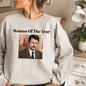 May include: Gray sweatshirt with the text "Woman Of The Year" and a picture of Ron Swanson from the TV show Parks and Recreation.
