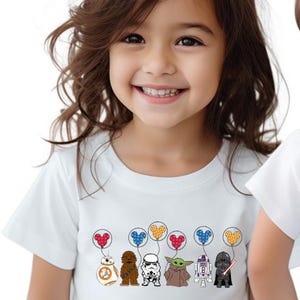 May include: White t-shirt featuring cartoon characters from Star Wars, including BB-8, Chewbacca, a Stormtrooper, Yoda, R2-D2, and Darth Vader. Each character is holding a balloon with a Mickey Mouse head design. The shirt is worn by a child.