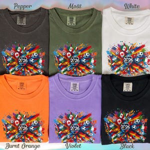 May include: Six t-shirts in various colors: pepper, moss, white, burnt orange, violet, and black. Each shirt features a colorful graphic with flags, soccer balls, and the text "2026 WORLD CUP".