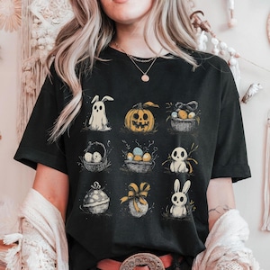 Può includere: T-shirt nero con una griglia di illustrazioni a tema pasquale. I disegni includono un coniglietto fantasma, una zucca, cestini di uova e altre grafiche pasquali. L'opera d'arte è in stile schizzato, con un'estetica vintage.