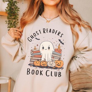 May include: A beige sweatshirt with a graphic of a ghost reading books with pumpkins and the text "Ghost Readers Book Club".