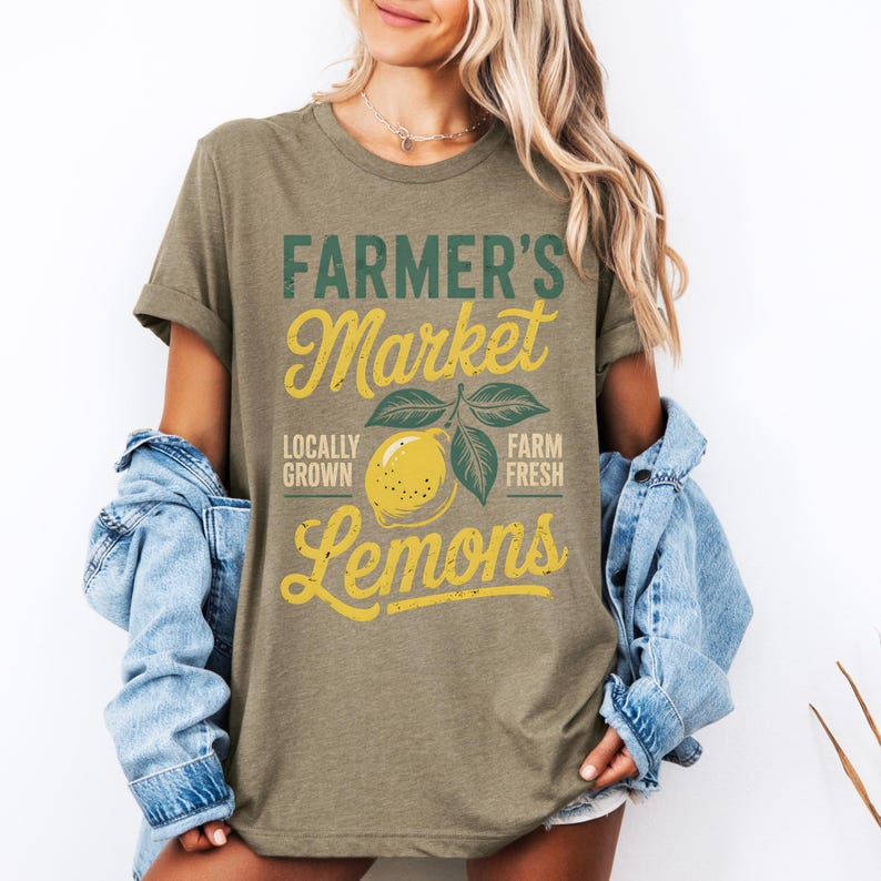 T-shirt with vintage-style “Farmer’s Market Lemons” graphic featuring a yellow lemon with leaves and rustic text. The main colors are yellow and green.