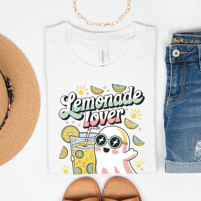 Peut inclure: T-shirt blanc avec l'inscription "Lemonade Lover" dans une police r&eacute;tro, repr&eacute;sentant un fant&ocirc;me de dessin anim&eacute; portant des lunettes de soleil et tenant un verre de limonade. Le motif comprend des tranches de citron et des &eacute;clats de soleil.