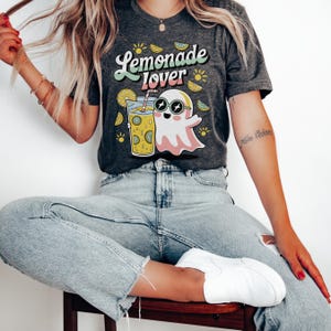 Peut inclure: T-shirt gris fonc&eacute; avec l'inscription "Lemonade Lover" dans une police r&eacute;tro. Le t-shirt pr&eacute;sente un fant&ocirc;me de dessin anim&eacute; portant des lunettes de soleil et tenant un verre de limonade. Des graphiques de citron et de soleil sont &eacute;galement inclus.