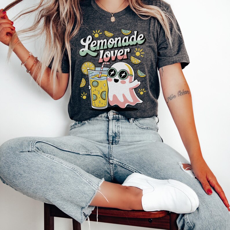 Peut inclure: T-shirt gris fonc&eacute; avec l'inscription "Lemonade Lover" dans une police r&eacute;tro. Le t-shirt pr&eacute;sente un fant&ocirc;me de dessin anim&eacute; portant des lunettes de soleil et tenant un verre de limonade. Des graphiques de citron et de soleil sont &eacute;galement inclus.