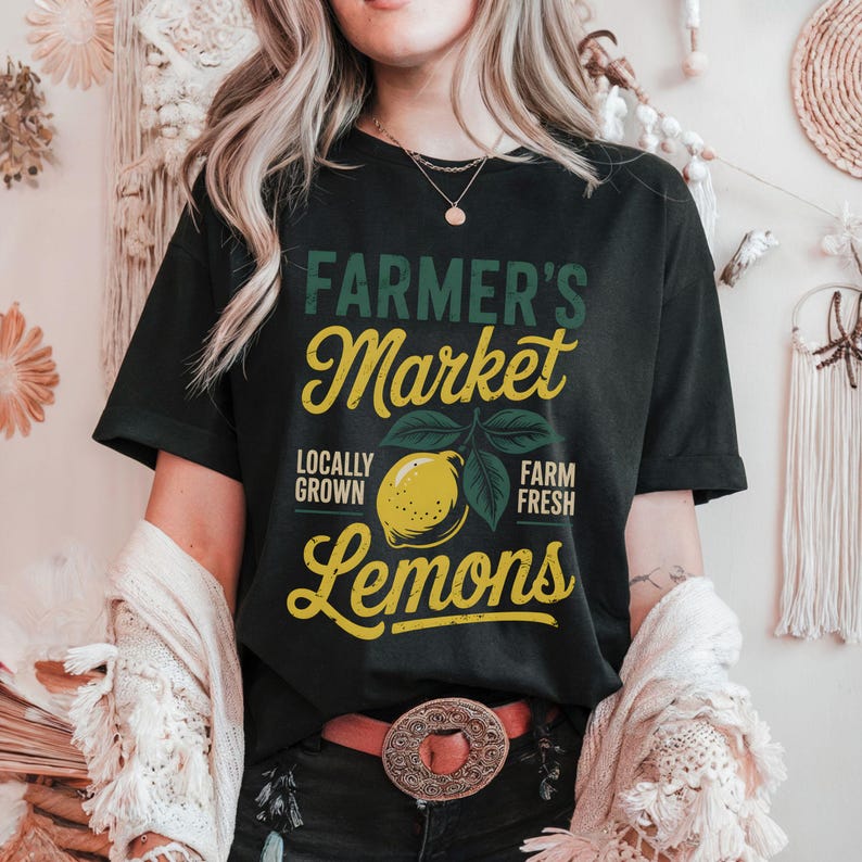 T-shirt with vintage-style “Farmer’s Market Lemons” graphic featuring a yellow lemon with leaves and rustic text. The main colors are yellow and green.