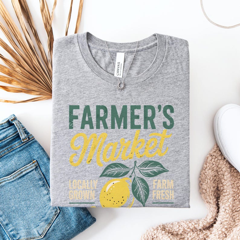 T-shirt with vintage-style “Farmer’s Market Lemons” graphic featuring a yellow lemon with leaves and rustic text. The main colors are yellow and green.
