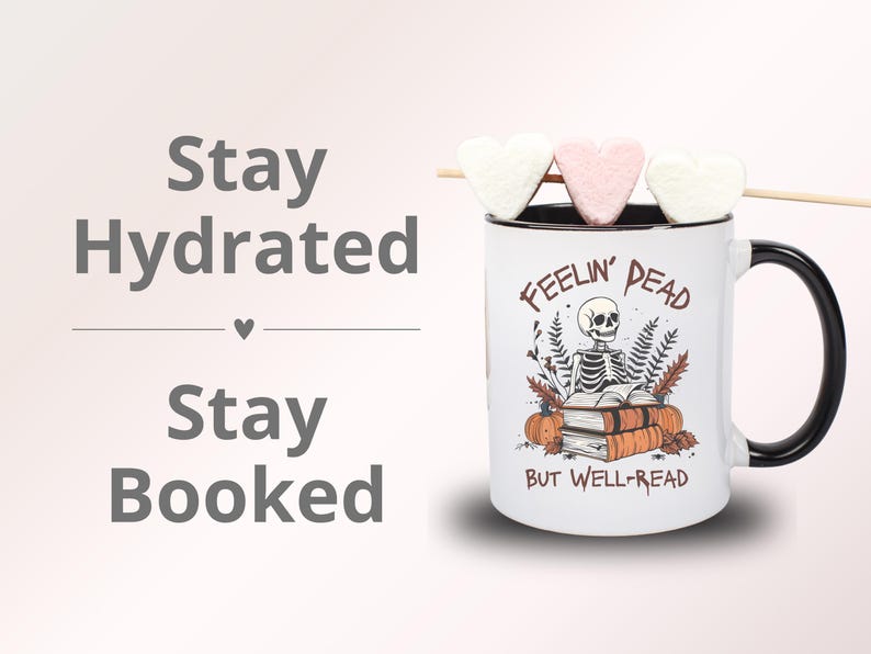 A white mug with a black or pink handle featuring a skeleton reading a book, surrounded by fall leaves and pumpkins, with the text: Feelin' Dead But Well-Read. Main colors are brown and orange.