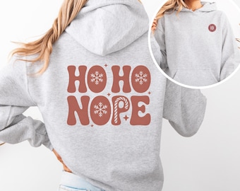 May include: A light gray hoodie with the words "HO HO NOPE" in a retro font on the back. The design includes snowflakes and a candy cane. A smaller snowflake design is on the front. The hoodie has a kangaroo pocket and a hood.