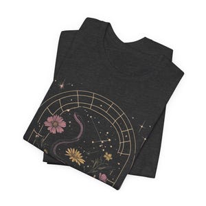 T-shirt featuring books, flowers, a snake, and stars framed by a mystical arched window—celestial, witchy, and dark academia styled.