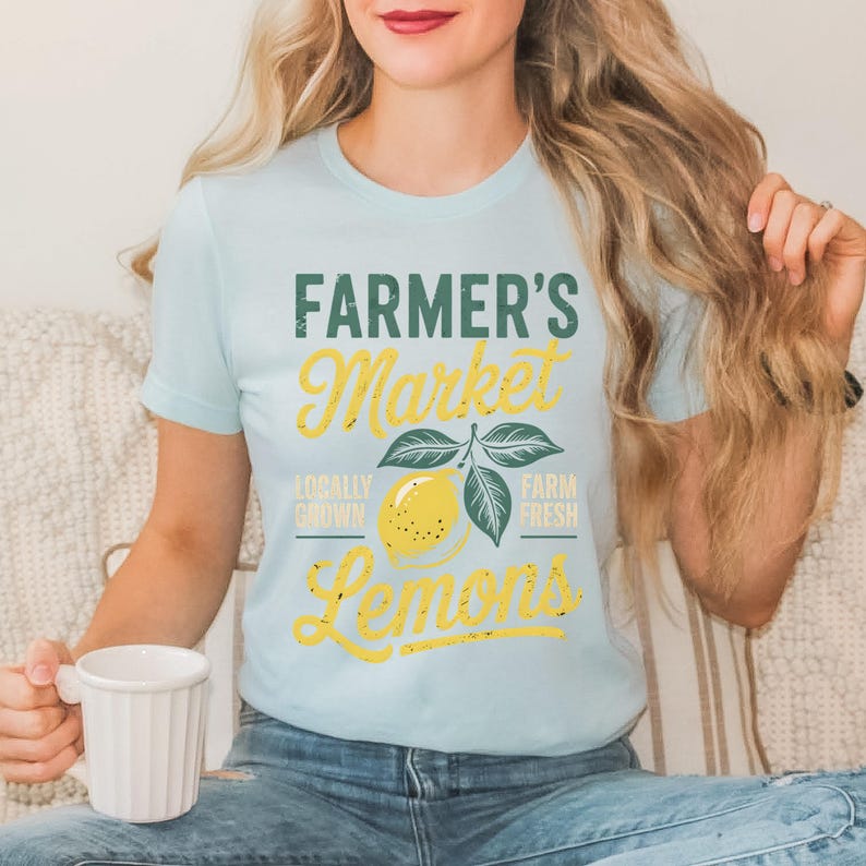 T-shirt with vintage-style “Farmer’s Market Lemons” graphic featuring a yellow lemon with leaves and rustic text. The main colors are yellow and green.