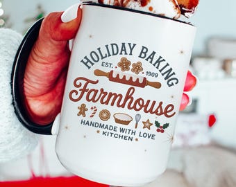 May include: White ceramic mug with a black rim, filled with marshmallows and chocolate. The mug features the text "HOLIDAY BAKING Farmhouse" with baking-themed illustrations. The mug is held by a person.