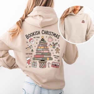 Op de afbeelding: Beige hoodie met een kerstthema ontwerp. De achterkant toont "Bookish Christmas" met een kerstboom gemaakt van boeken en andere vakantie-illustraties. Een kleinere versie van de boekenboom staat op de voorkant.