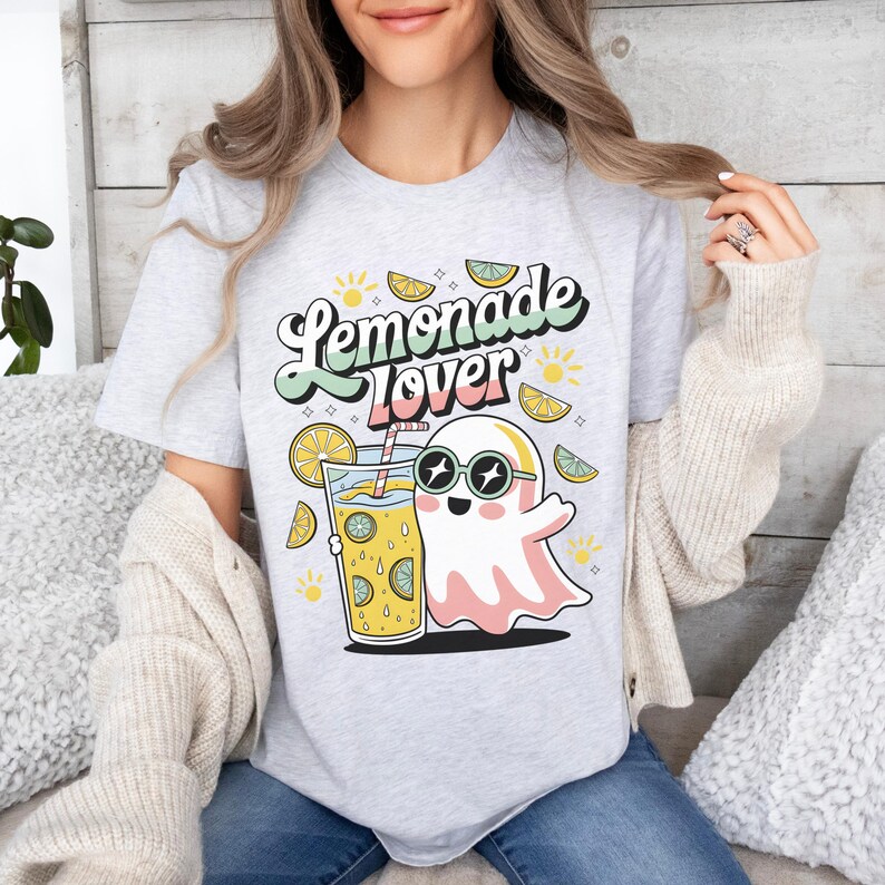 Peut inclure: T-shirt gris clair avec l'inscription "Lemonade Lover" dans une police r&eacute;tro. Le t-shirt pr&eacute;sente un fant&ocirc;me de dessin anim&eacute; portant des lunettes de soleil et tenant un verre de limonade. Des illustrations de citron et de soleil sont &eacute;galement pr&eacute;sentes.