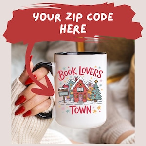 May include: White ceramic mug with a black handle and rim, featuring a colorful illustration of a town scene with houses, a Christmas tree, and the words "Book Lovers Town". The mug also has the text "Your Zip Code Here".