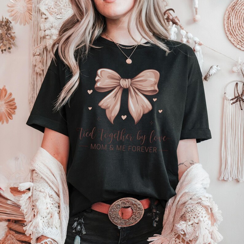 A sentimental t-shirt featuring a beautifully illustrated silk bow with the phrase: Tied Together by Love – Mom & Me Forever. Small hearts surround the design, making it a sweet and emotional tribute to the mother-daughter bond. The colors are very soft and all in pink tones.