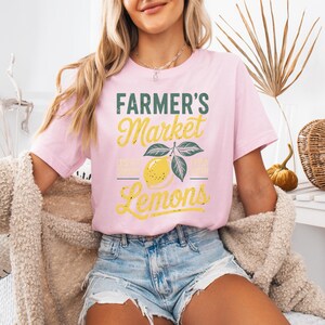 T-shirt with vintage-style “Farmer’s Market Lemons” graphic featuring a yellow lemon with leaves and rustic text. The main colors are yellow and green.
