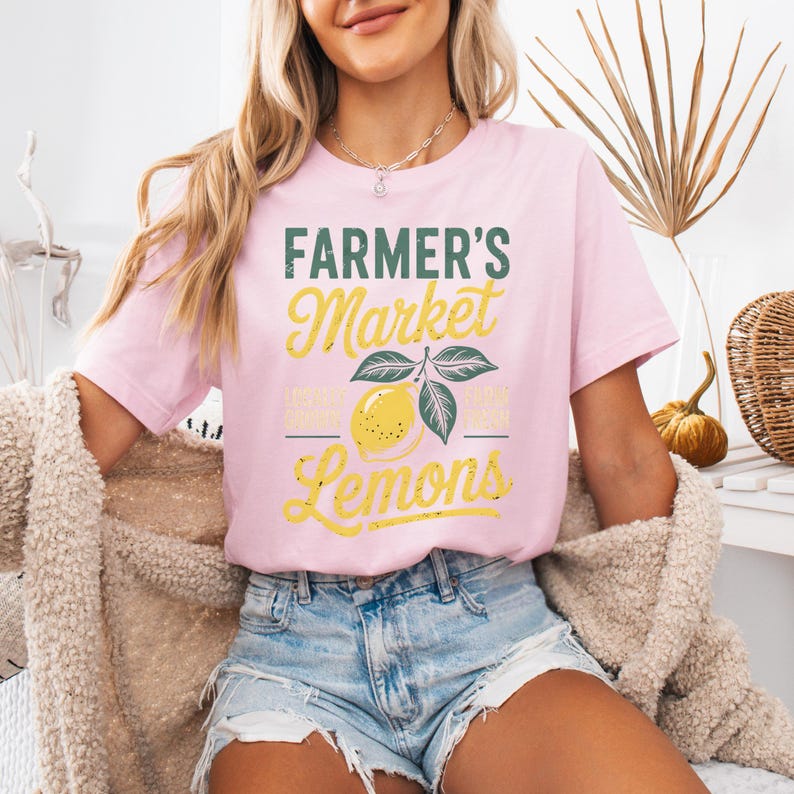 T-shirt with vintage-style “Farmer’s Market Lemons” graphic featuring a yellow lemon with leaves and rustic text. The main colors are yellow and green.