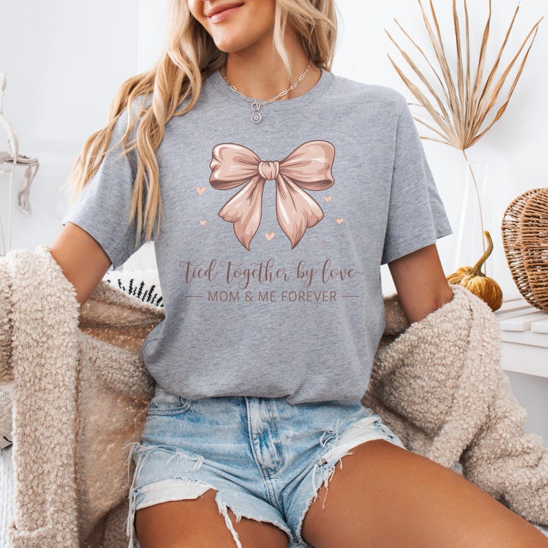A sentimental t-shirt featuring a beautifully illustrated silk bow with the phrase: Tied Together by Love – Mom & Me Forever. Small hearts surround the design, making it a sweet and emotional tribute to the mother-daughter bond. The colors are very soft and all in pink tones.