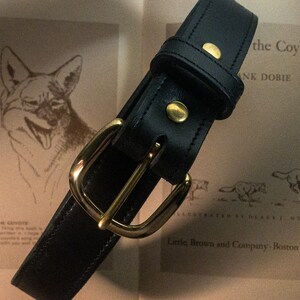 May include: A black leather belt with a gold buckle. The belt is lying on a book with the text "the Coyote" and "Little, Brown and Company, Boston - 1949".