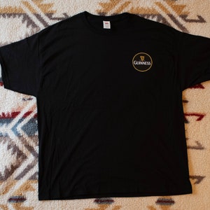 Puede incluir: Camiseta negra con el logo de Guinness en el pecho izquierdo. El logo es un c&iacute;rculo dorado con el s&iacute;mbolo del arpa Guinness y la palabra "Guinness" en blanco. La camiseta es de tejido suave.