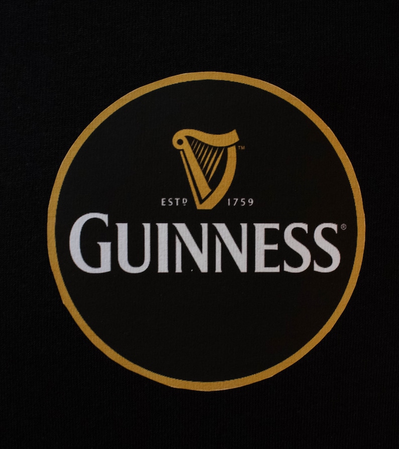 Puede incluir: C&iacute;rculo negro con borde dorado que muestra el logotipo de Guinness. El logotipo incluye un arpa dorada, la palabra "GUINNESS" en blanco y el texto "ESTD 1759".