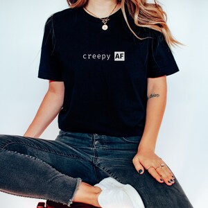 May include: A black t-shirt with the text "creepy AF" printed in white on the front.