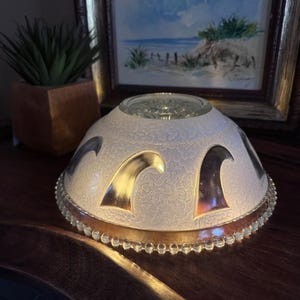May include: A vintage, frosted glass lampshade with a decorative pattern and gold accents. The lampshade features a scalloped edge and a clear glass top. The design includes wave-like shapes in gold and silver.