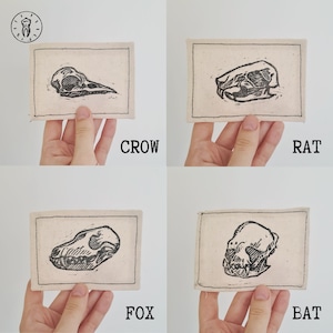 May include: Four embroidered patches featuring black and white illustrations of animal skulls. The patches are on a white background and are labelled "CROW", "RAT", "FOX", and "BAT".