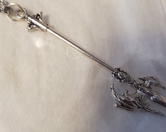 May include: Silver-toned necklace with a detailed spear pendant. The spear has a long, thin shaft and a three-pronged tip with intricate designs.