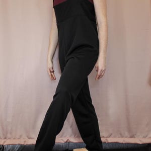 Könnte beinhalten: Ein schwarzer ärmelloser Jumpsuit mit weitem Bein. Der Jumpsuit hat ein schlichtes Design und ist aus einem weichen, bequemen Stoff gefertigt.