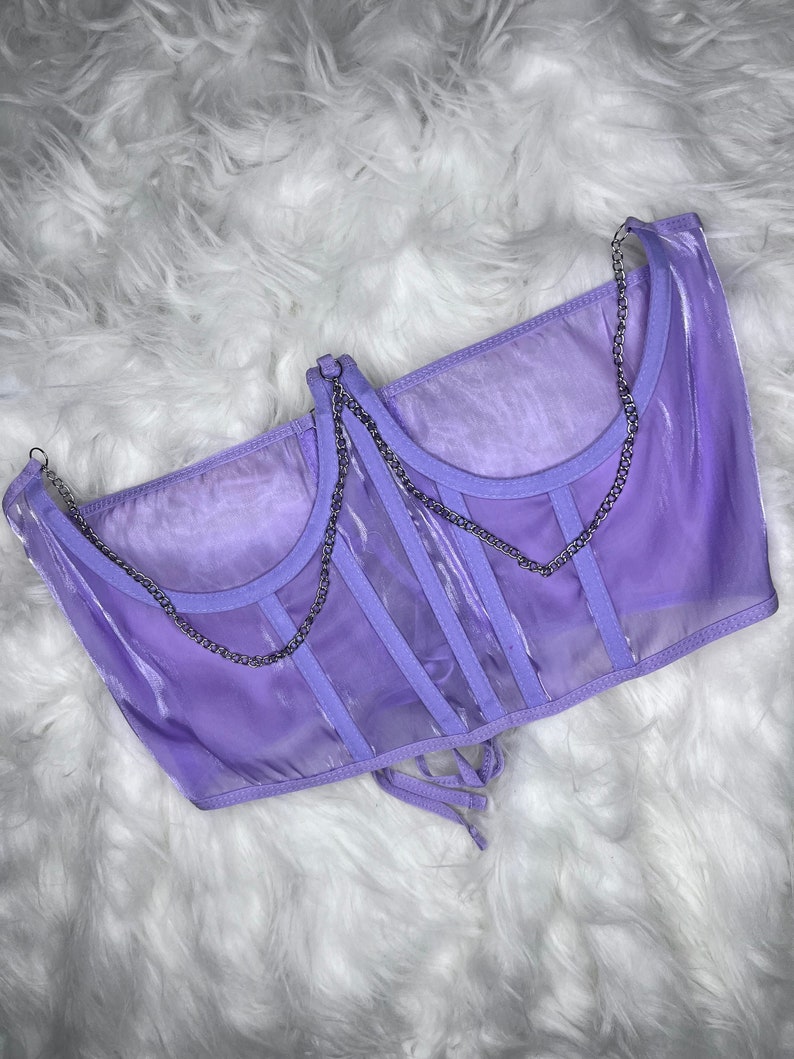 Op de afbeelding: Een lavendelkleurig doorschijnend corsettop met zilveren kettingbandjes en een veter aan de achterkant.
