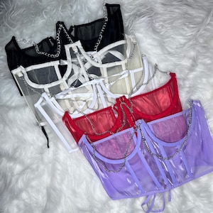 Op de afbeelding: Vijf doorschijnende mesh tops met kettingbandjes in verschillende kleuren: zwart, wit, cr&egrave;me, rood en paars. De tops zijn op elkaar gelegd, met de zwarte top onderaan en de paarse top bovenaan.