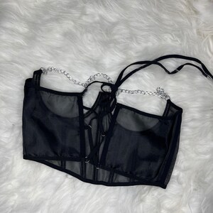 Op de afbeelding: Zwart mesh corset top met een veter aan de voorkant en een zilveren kettingdetail.