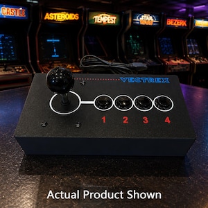 May include: A black Vectrex arcade controller featuring a single joystick with a round black knob, four black action buttons labelled 1, 2, 3, and 4 in red, and a white graphic line connecting the controls. The device includes a black power cord.