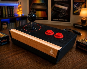 May include: A black Atari joystick with a wooden front panel, two red buttons, and a black joystick ball. The Atari logo is visible on the front. The text "Actual Product Shown" is at the bottom of the image. The joystick is on a wooden surface.