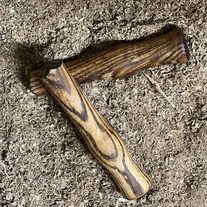 May include: Two wooden handles with a dark brown and light brown striped pattern. The handles are lying on a bed of wood shavings.