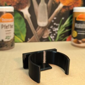 May include: A black plastic spice rack holder with a curved design. The holder is designed to hold round spice jars.