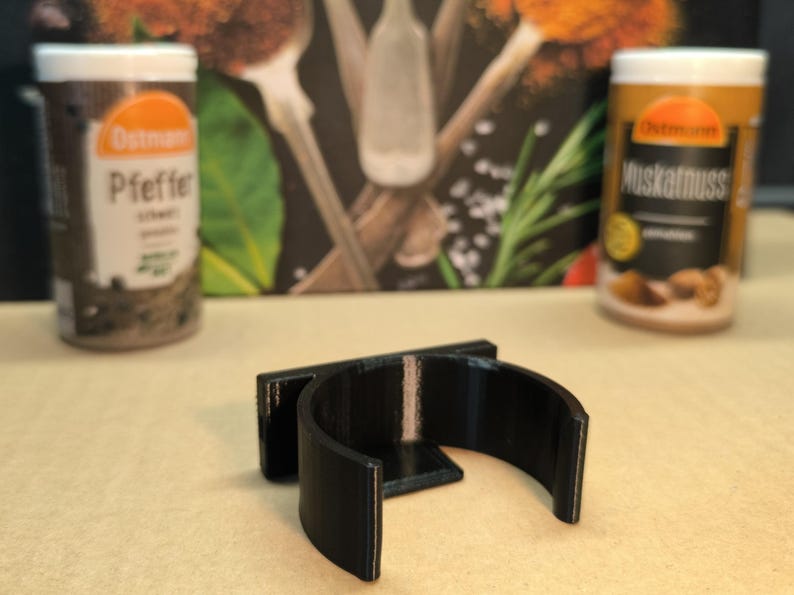 May include: A black plastic spice rack holder with a curved design. The holder is designed to hold round spice jars.