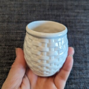 May include: White ceramic planter with a woven basket design. The planter is small and has a round shape.