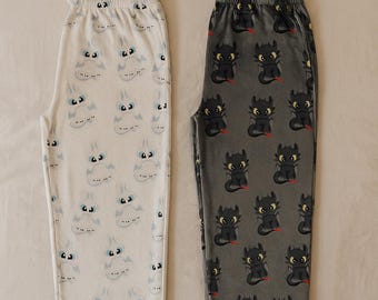 May include: Two pairs of pajama pants. One pair is white with a repeating pattern of a cartoon character with blue eyes. The other pair is gray with a repeating pattern of a black cartoon dragon with red accents.