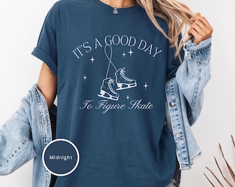 May include: A navy blue t-shirt with the text "It's a good day to figure skate" in white. The design includes a pair of white figure skates and stars.